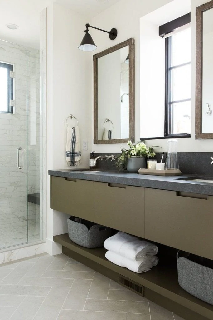 Benjamin Moore Tate Olive cabinets in a modern bathroom with white walls, wood mirrors and tiled shower.