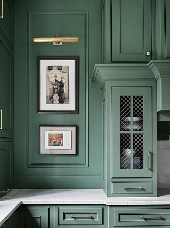 Farrow & Ball Green Smoke kitchen cabinet details with a brass light hung over artwork.