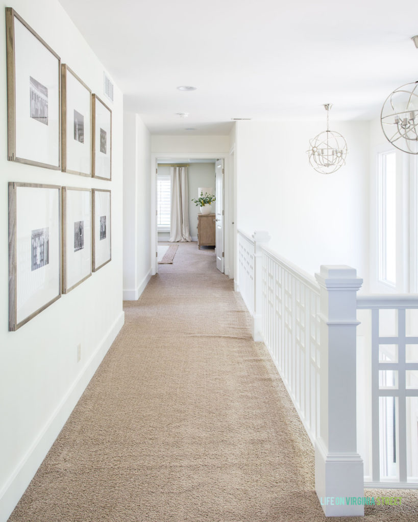 A photo gallery wall in a hallway with walls painted Benjamin Moore Simply White and silver orb chandeliers.