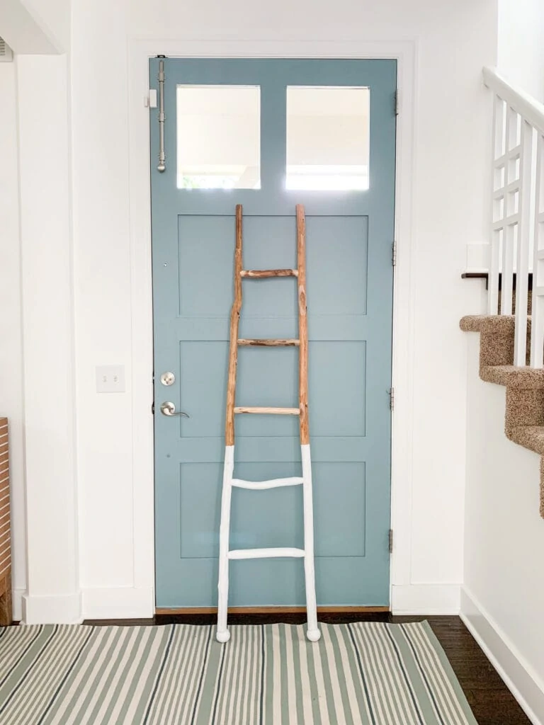 A coastal style entryway with Simply White Walls, Water's Edge painted door, striped rug, and a paint dipped wood ladder.