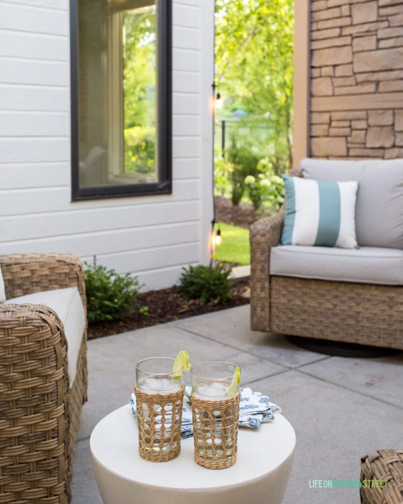 Outdoor dining in a courtyard with wicker chairs, white table, cane drinking glasses and bright green trees.