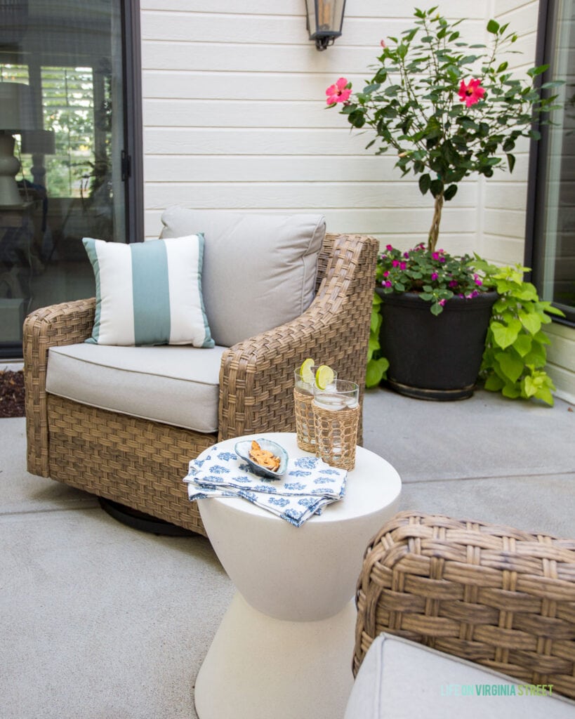 Cozy outdoor patio furniture including natural woven chairs, concrete side table, block print napkins, cane drinking glasses and more in an outdoor courtyard area.