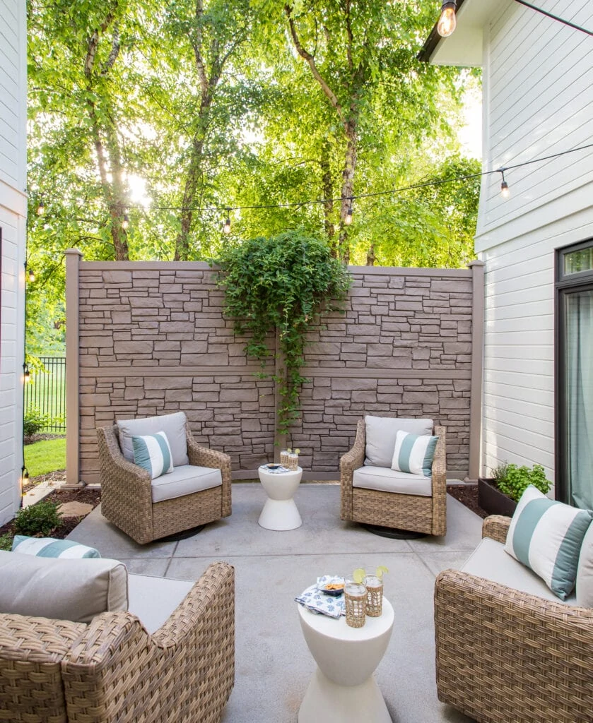 An outdoor courtyard with faux stone wall, wicker chairs, white side tables and blue and white striped pillows.