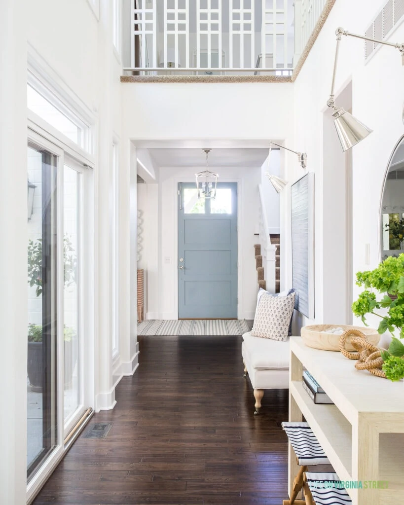 An entryway hallway with blue gray interior door, raffia console table, silver swing arm scones, and dark hardwood floors.