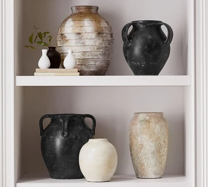 A collection of weathered vases styled on a bookshelf.