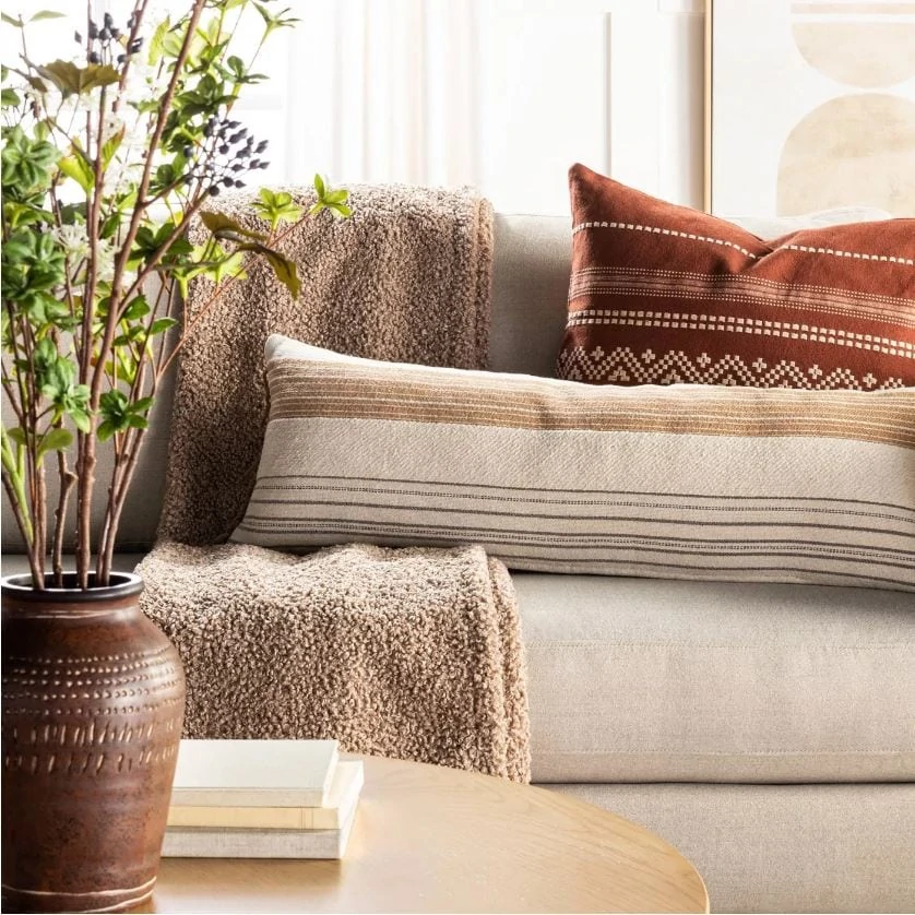 A cozy fall sofa filled with a boucle throw blanket, oversized striped lumbar pilllow, and embroidered pillow and abstract wall art in the background.