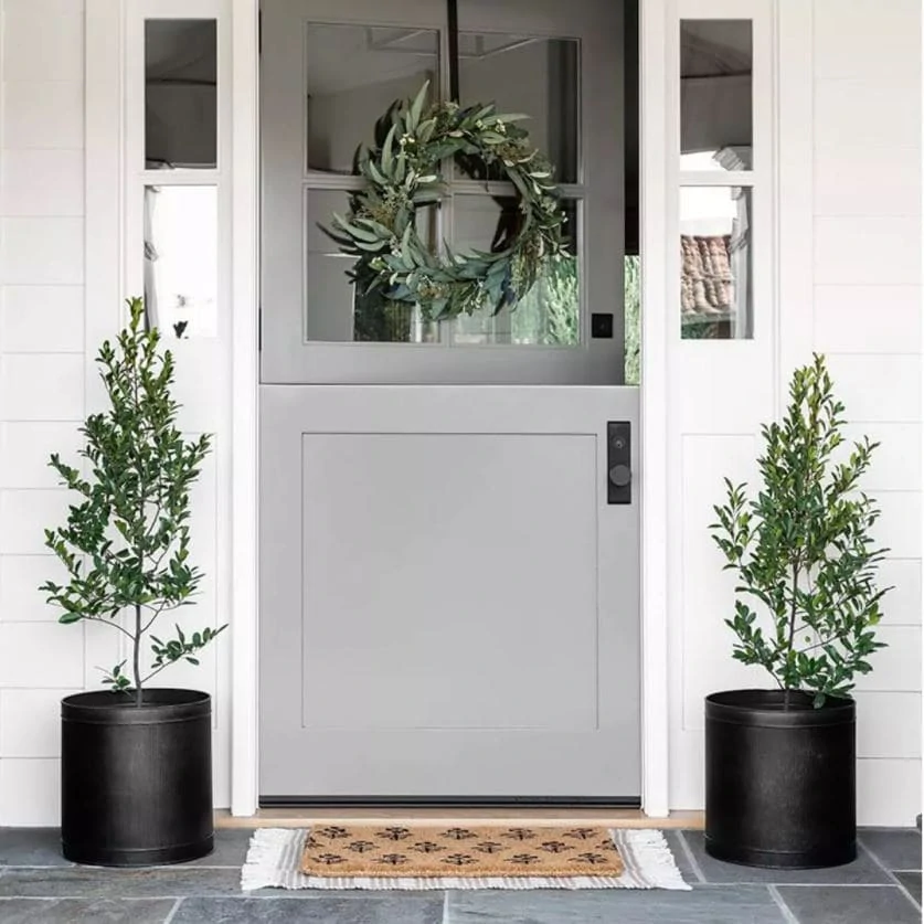 A cute front porch with gray Dutch door, black planters, faux eucalyptus wreath, block print doormat and a striped outdoor rug.