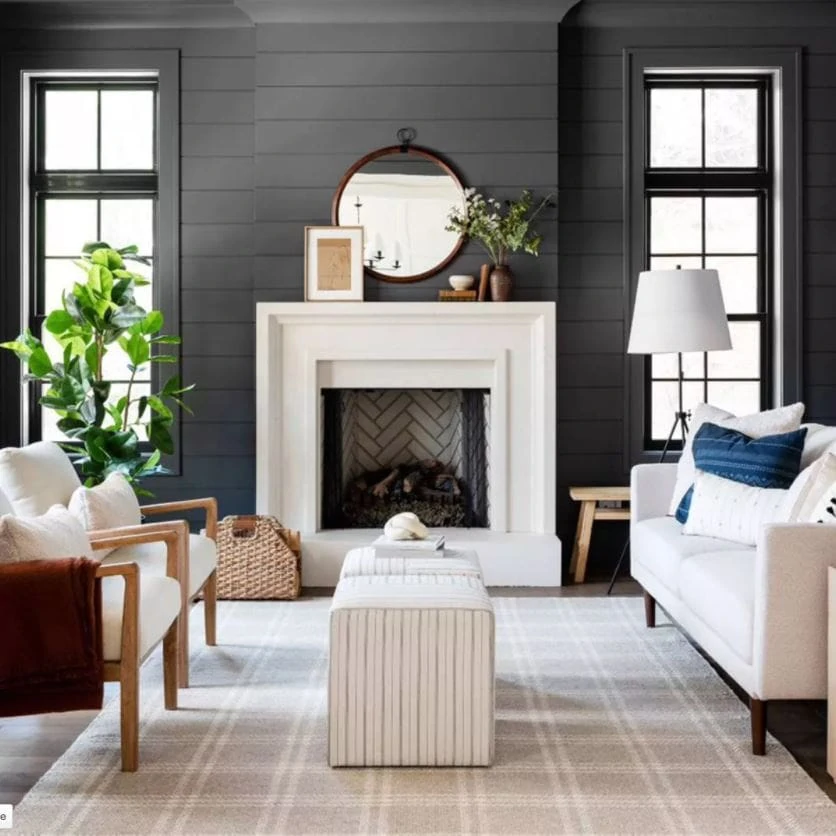 Some of the best finds from the w Studio McGee fall collection at Target! Shown here in a moody living room with dark shiplap, tan plaid rug, striped ottoman cubes, a round mirror over the fireplace with leaning art, wood and upholstery chairs, a faux rubber tree, and an oversized tripod lamp.