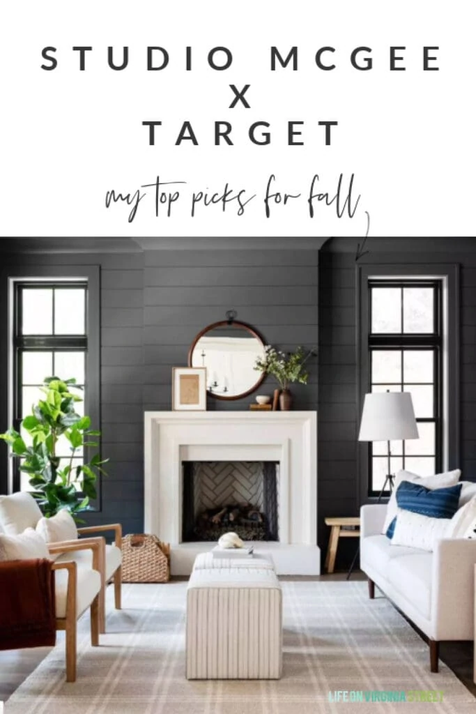 A dark shiplap living room with tan plaid rug, striped ottoman cubes, a round mirror over the fireplace, wood and upholstery chairs, a faux rubber tree, and an oversized tripod lamp.