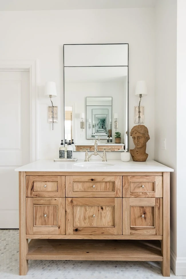 Loving these small bathroom ideas, including this wood vanity, small hex marble tile floors, silver sconce lights, and a tall thin black frame mirror.