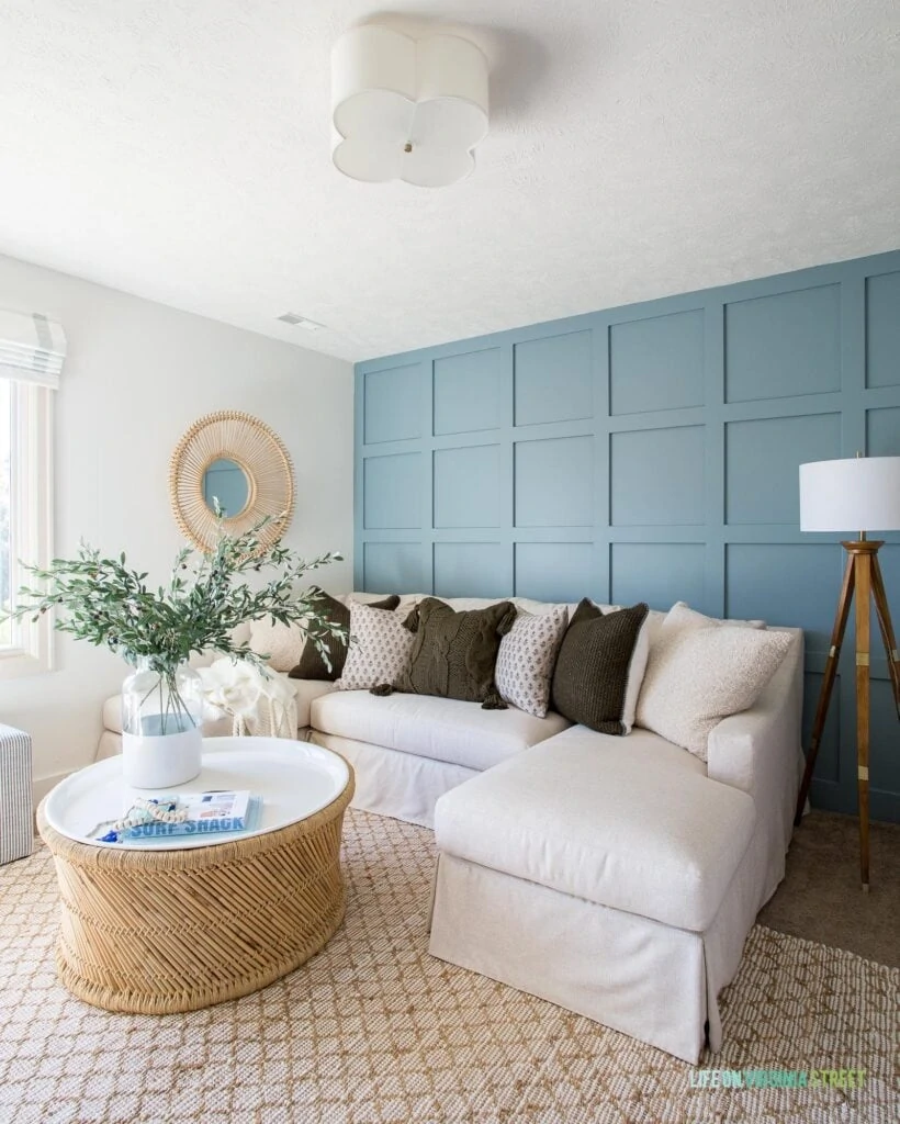 A den with blue board and batten wall, jute rug, scallop light, round coffee table and linen sectional.