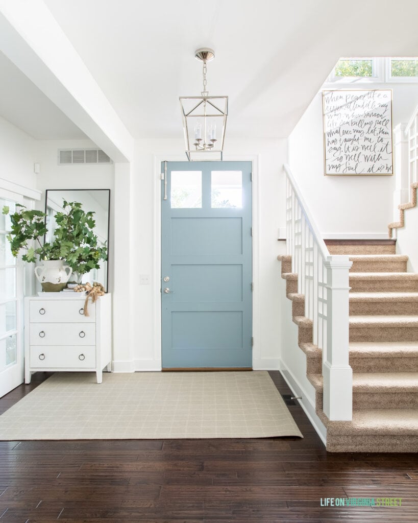 2020 fall home tour with a fall entryway that includes white walls, blue front door, plaid rug, maple leaves and a white cabinet.