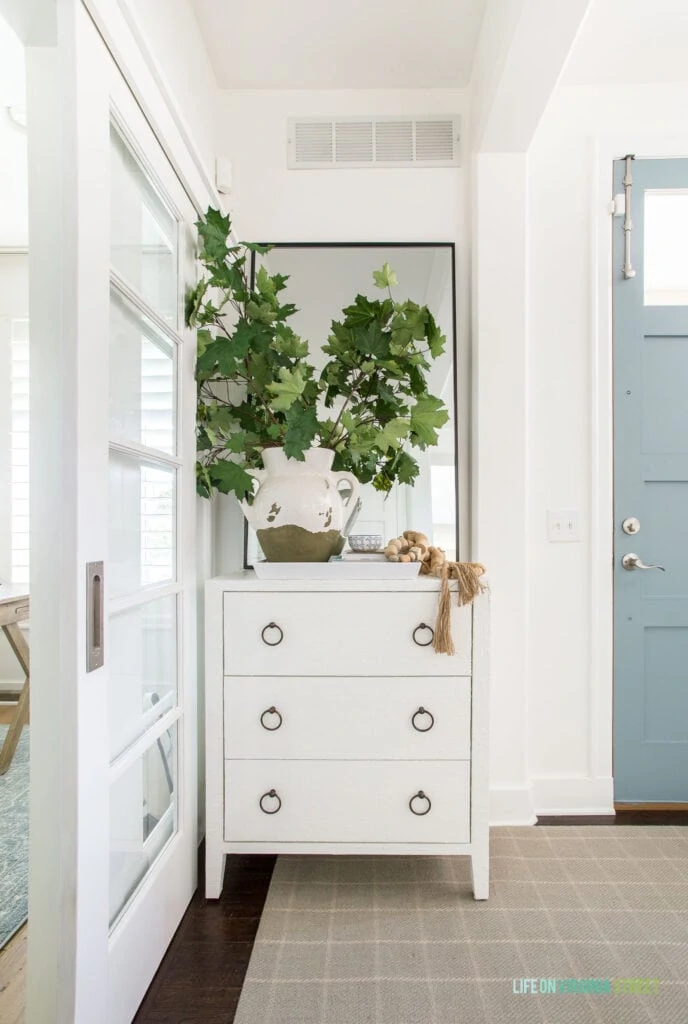 A white raffia cabinet with drawers styled in a fall entryway as part of a 2020 fall home tour.
