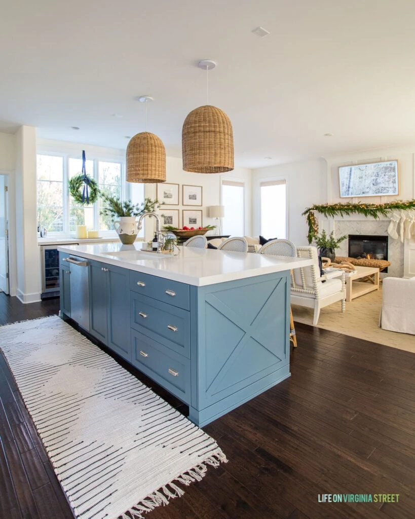 Our 2020 Christmas home tour featuring our kitchen with a blue island, ivory and black runner rug, basket pendant lights, and a wreath on the window.