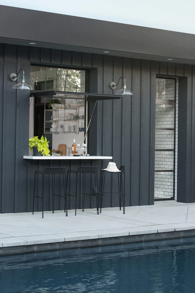 Pool house with black vertical board and batten, an outdoor bar countertop, and a dark pool.