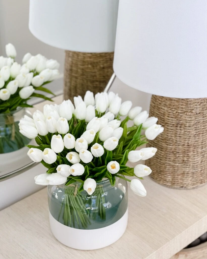Faux white tulips in a paint dipped vase on a raffia console table. Includes other spring decorating ideas that are available on Amazon!