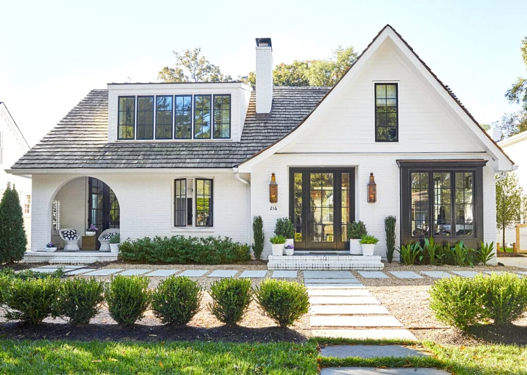 White painted brick home with black window trim, copper lanterns and an arched porch.