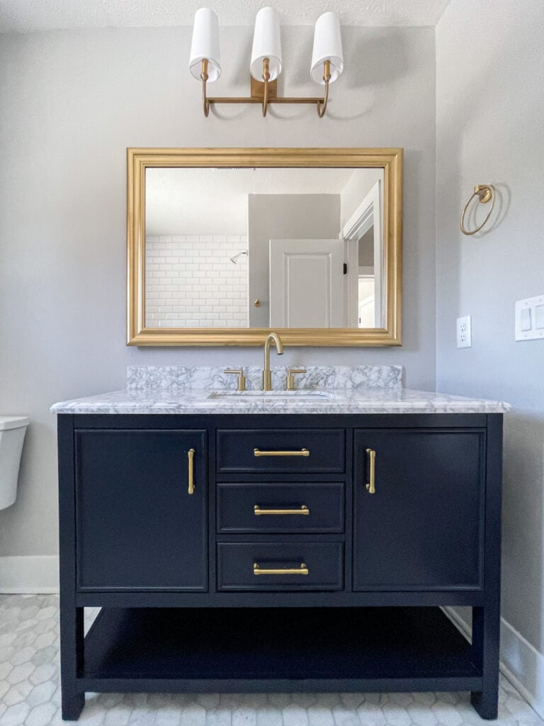 Navy blue vanity with gold hardware and marble hex flooring.