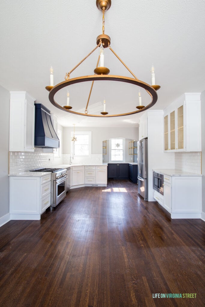 Tudor house renovation with dark hardwood floors, white kitchen cabinets, Sherwin Williams Naval range hood and lower kitchen cabinets, and a large wagon wheel light fixture.