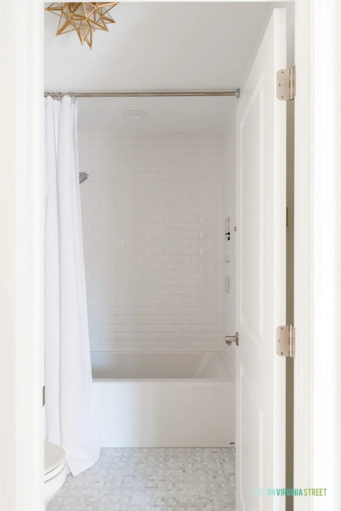 Jack & Jill Bathroom remodel reveal with white beveled subway tile over the tub, a gold Moravian star light fixtures, white waffle knit shower curtain, and Carrara marble tile floors.