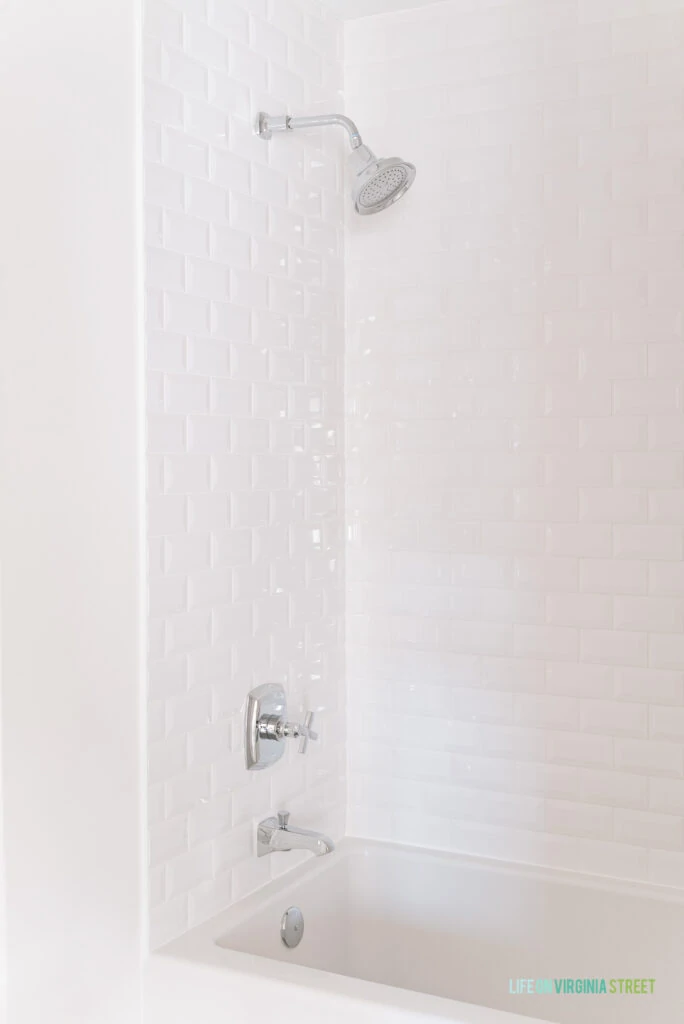 A remodeled shower tiled with white beveled subway tile and silver cross bath fixtures.