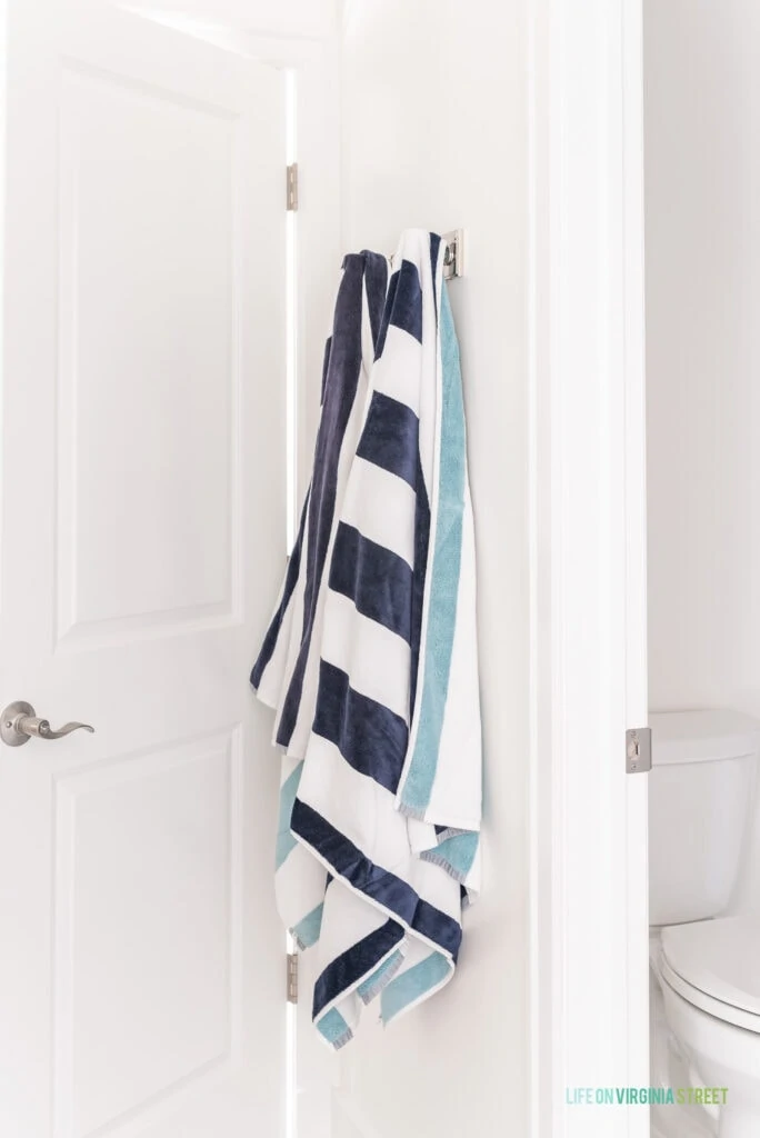 Robe hooks used in a bathroom to hold reversible blue striped pool towels.