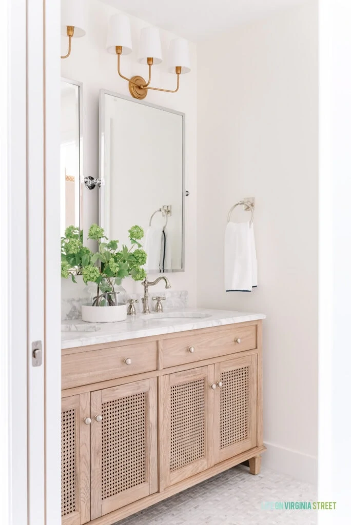 Jack & Jill Bathroom remodel reveal with Carrara marble pinwheel tile floors, a wood cane vanity, polished nickel pivot mirrors, and gold bathroom sconces.