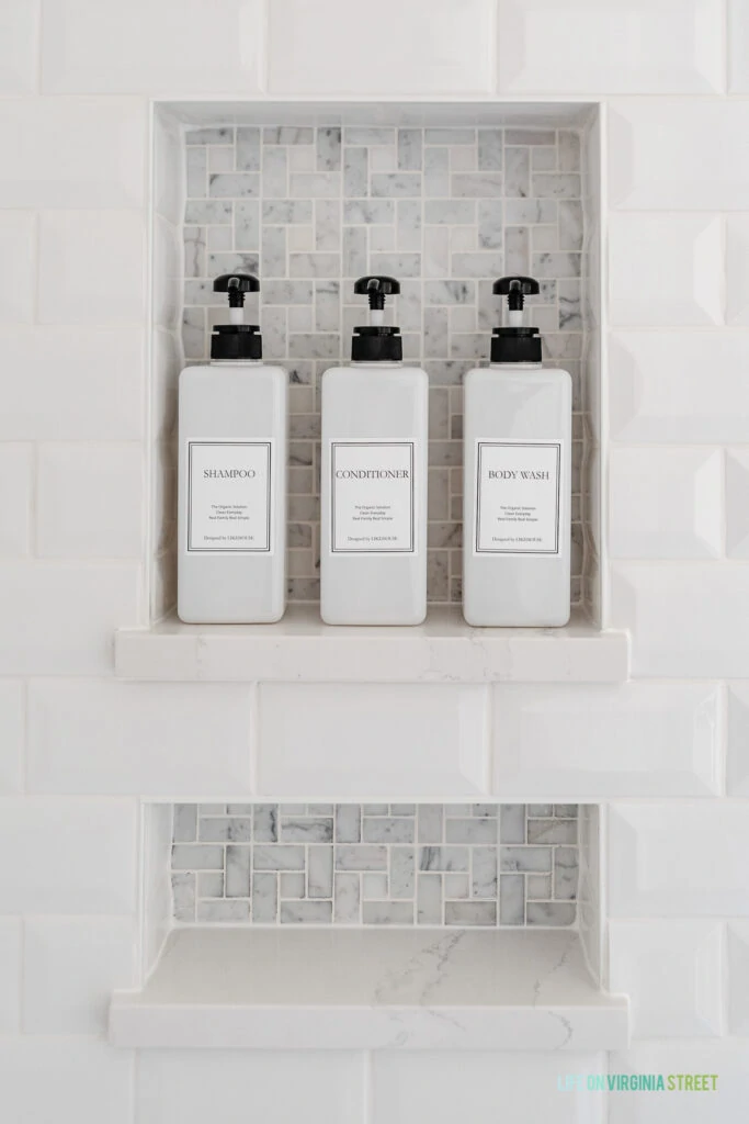 A bathroom shower niche with white beveled subway tiles, marble pinwheel tile, Silestone ledge shelf for shampoo bottles, and a lower niche to hold bar soap and razors.