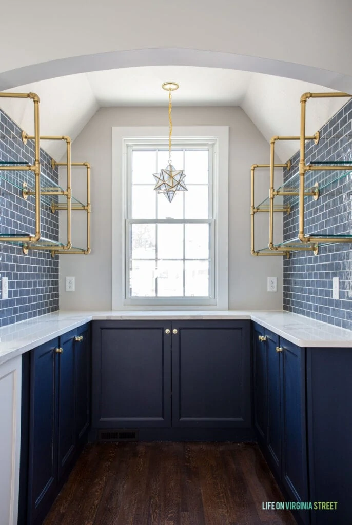 A butler's pantry with lower cabinets painted Sherwin Williams Naval, along with brass open shelving, navy blue subway tile, and a Moravian star pendant light fixture.