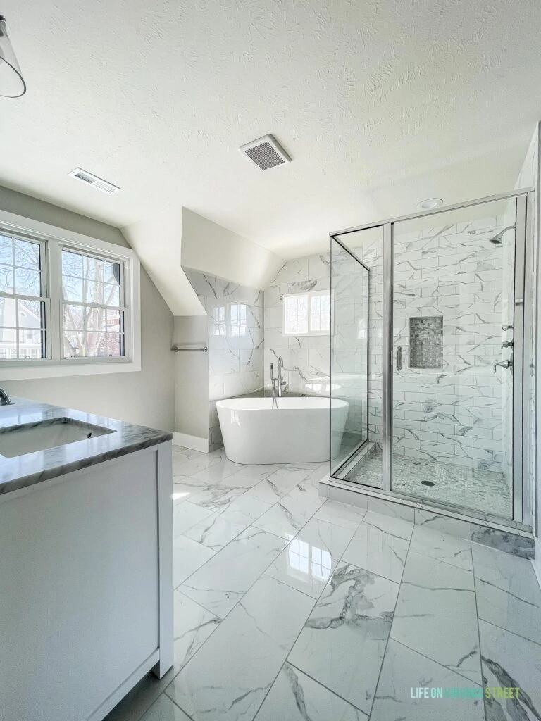 Master bathroom with affordable ceramic tile that looks like Carrara marble! Includes a soaking tub, large glass framed shower, and white double vanity.