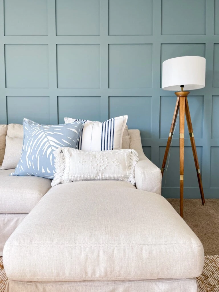 Serena & Lily summer pillows on a linen sectional with a blue board and batten wall and tripod floor lamp.