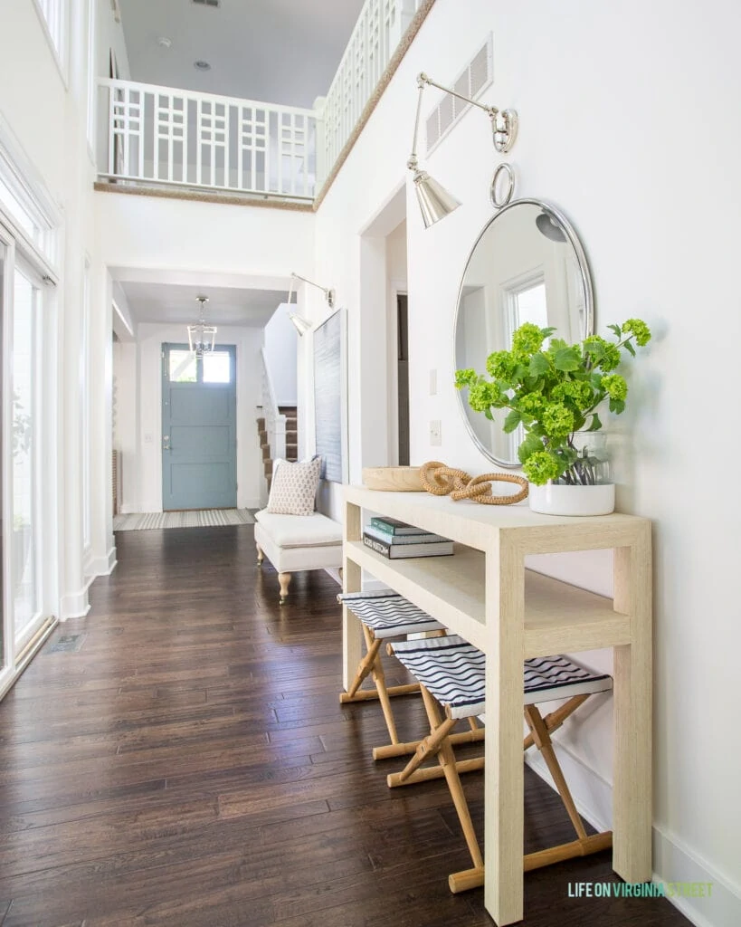 Entryway hallway with a raffia console table, striped stools, round mirror, and blue interior front door.