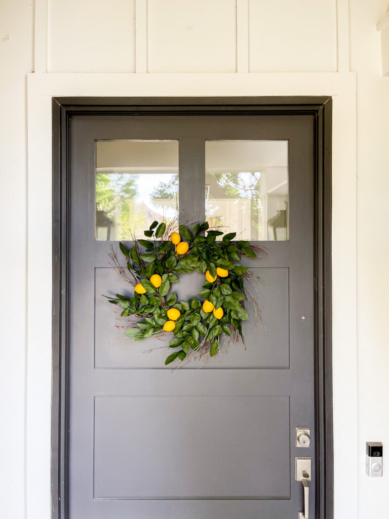 A lemon wreath on a dark brown front door and white house with board and batten siding.