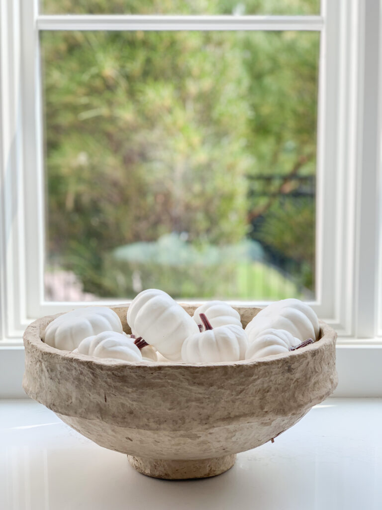 A paper mache bowl filled with faux white pumpkins.
