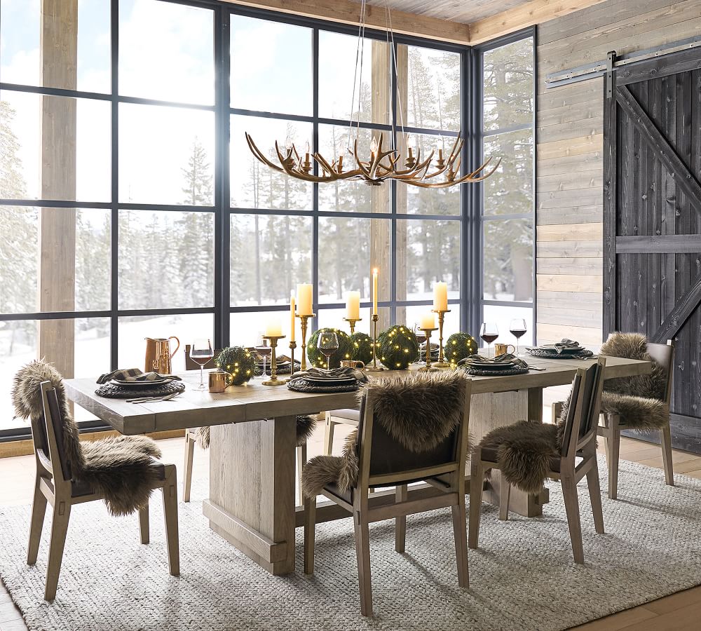 A beautiful rustic Christmas dining scene with faux greenery orbs, antler chandelier and light wood furniture.
