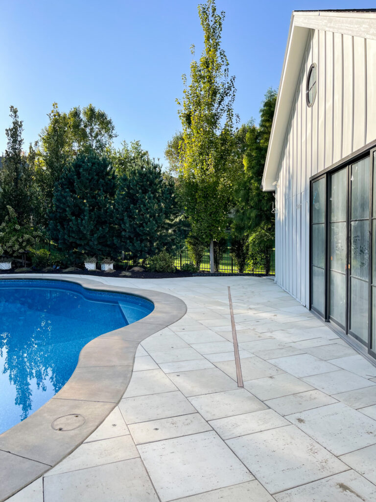 An in-ground channel drain installed between a swimming pool and a house.