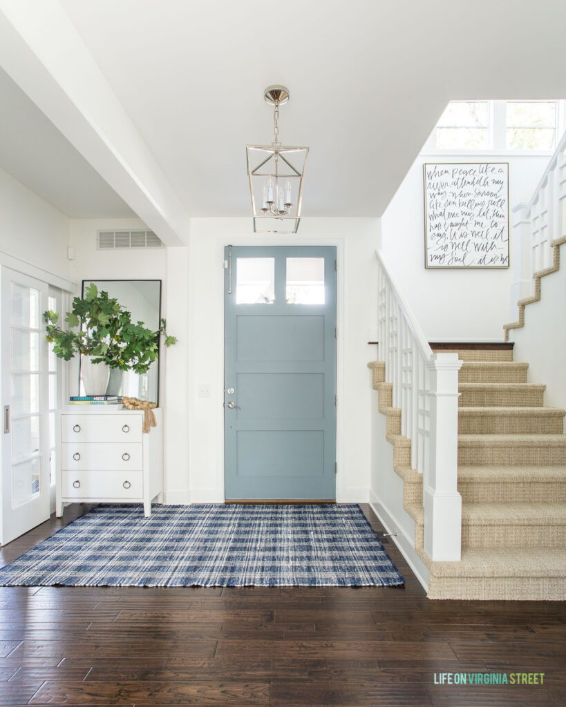 An entryway decorated for fall with a white raffia cabinet, maple leaves, and a blue interior door painted Benjamin Moore Water's Edge.