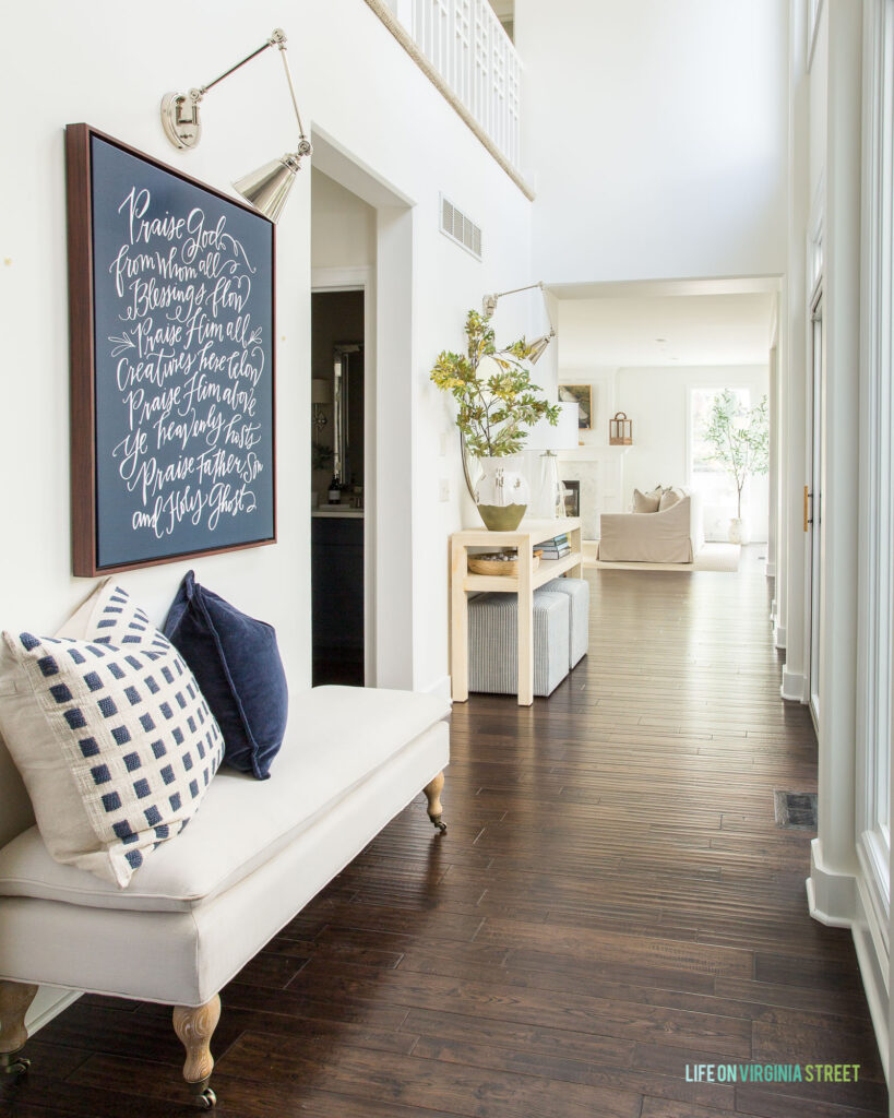 A fall hallway decorated with a Doxology canvas, raffia console table, faux oak leaves, and shades of navy blue and ivory.