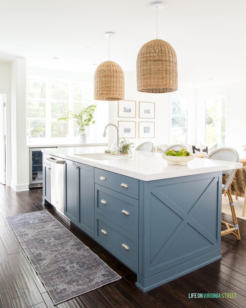 A machine washable runner rug in a kitchen with a blue island, basket pendant lights, and a large bright window.
