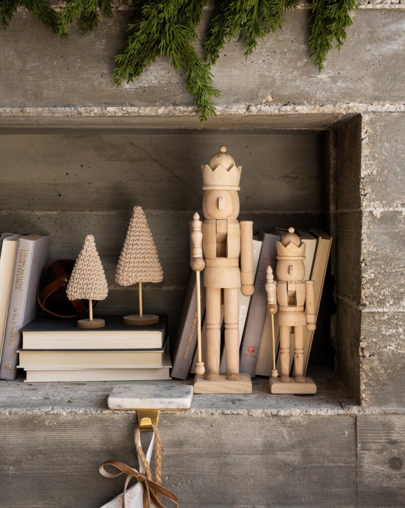 Natural wooden nutcrackers styled on a fireplace with knit Christmas trees and a stocking holder.