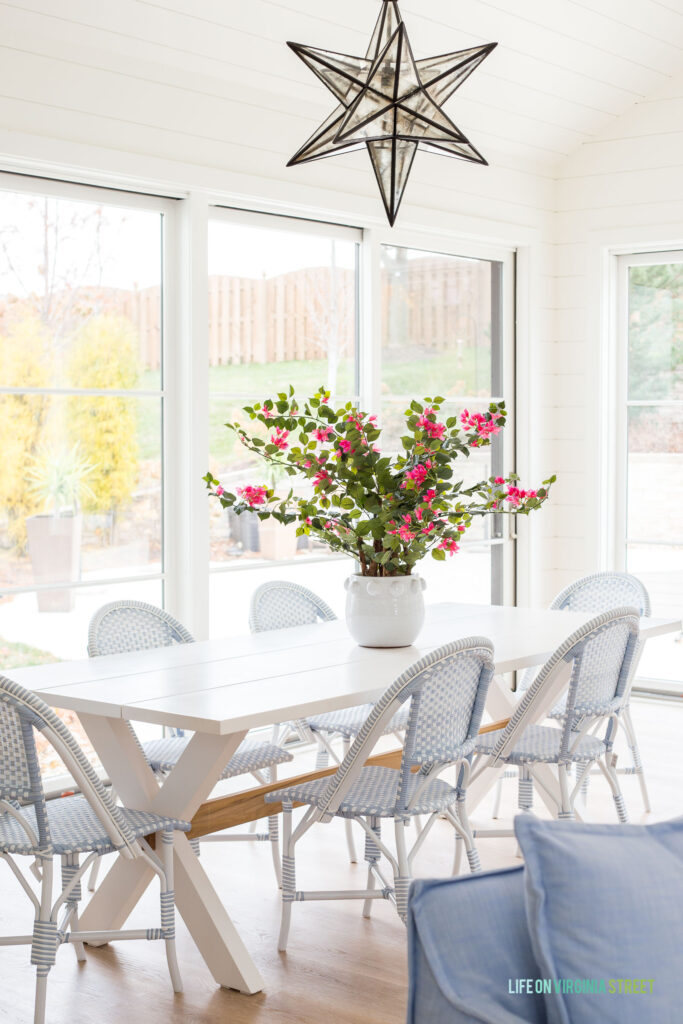 A pool house dining room with a white dining table, bistro chairs, a large Moravian star pendant light and a bright pink bougainvillea plant on the table.