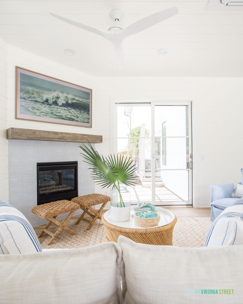 A simple fireplace in our pool house includes white shiplap walls, blue and white Annie Selke tile, Serena & Lily furniture and a Frame TV displaying ocean art.