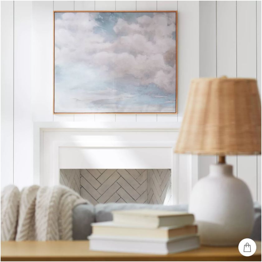 Oversized cloud art hung over a white plaster fireplace mantel.