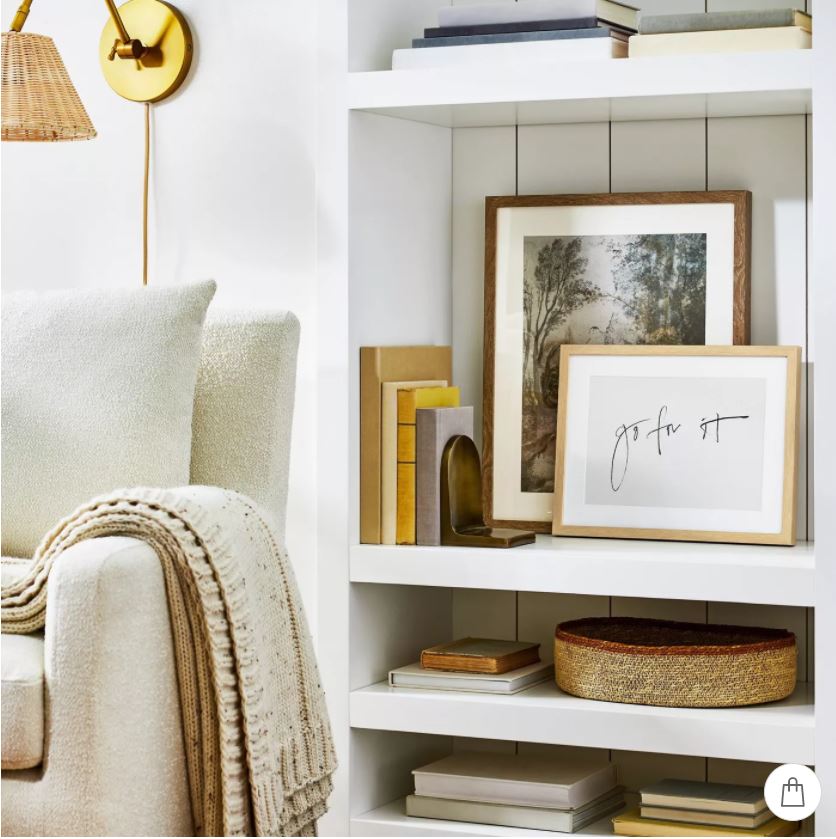 A reading nook with a boucle chair, seagrass swing arm sconce light, layered art, and stacked books.