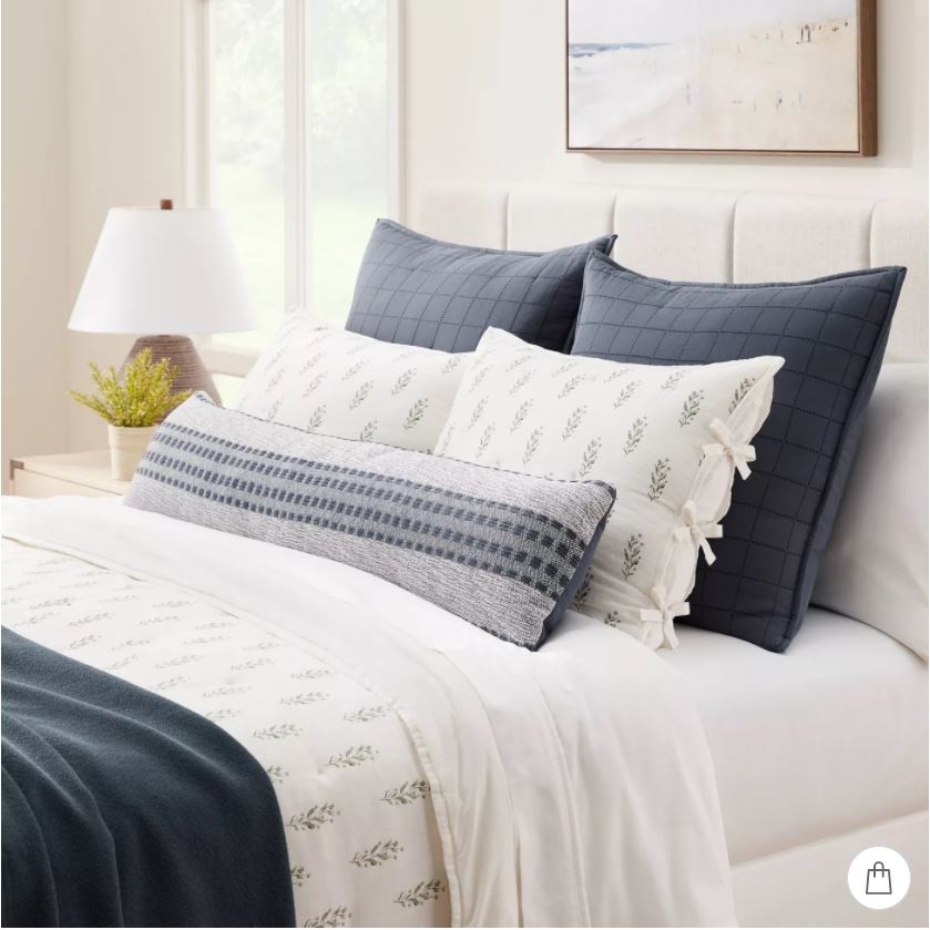 Beautiful layered bedding with navy blue Euro shams, block print shams, a long woven striped lumbar pillow and beach art.