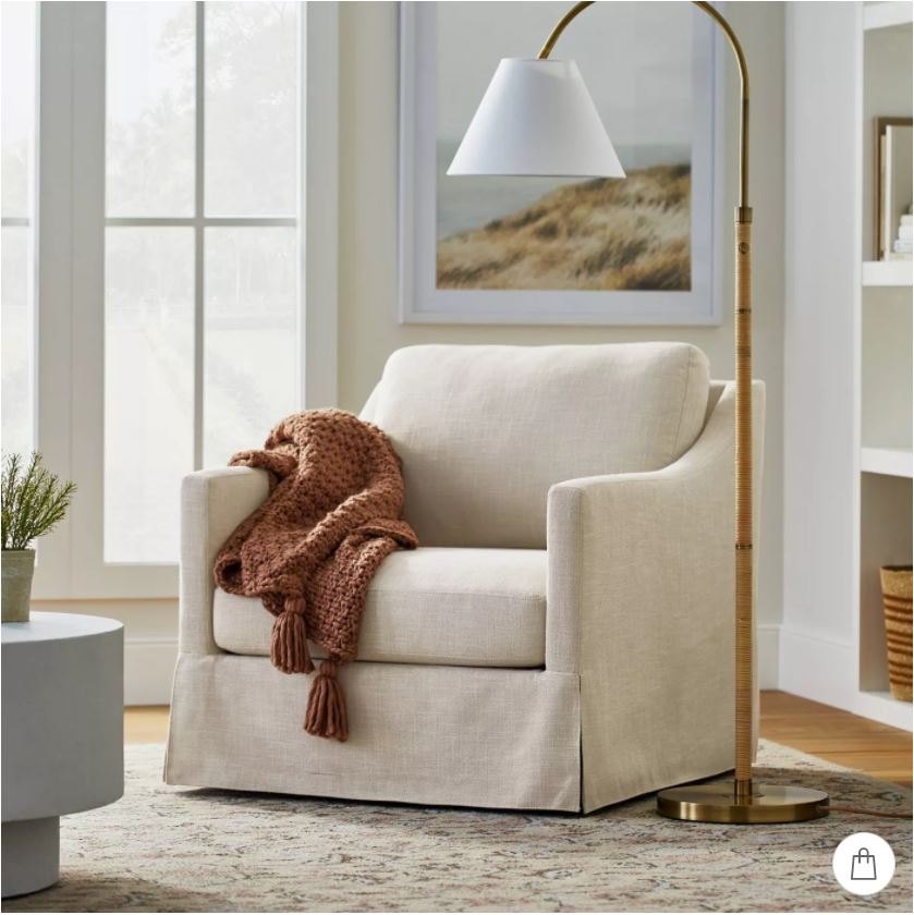 An upholstered swivel armchair with a rattan wrapped arc floor lamp.