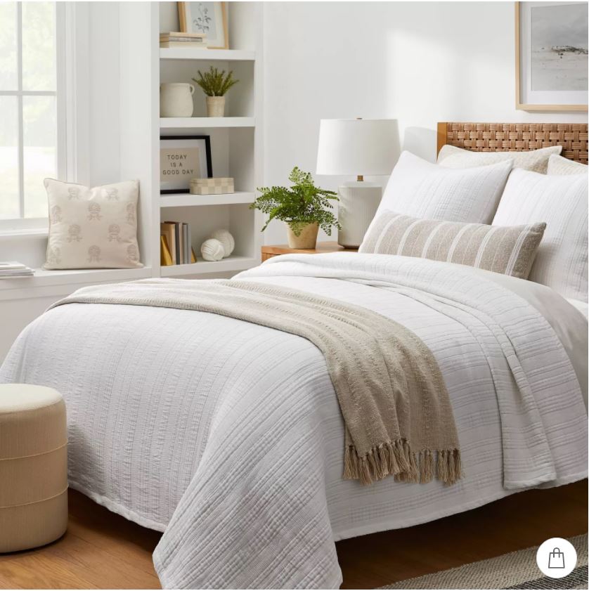 A bedroom with a woven headboard, white quilted bedding, cozy layers and simple accessories!