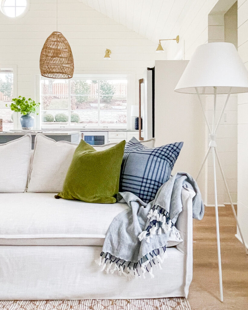 A pool house living room decorated in neutral, blue and green decor, with a white tripod lamp from the new Studio McGee collection at Target!