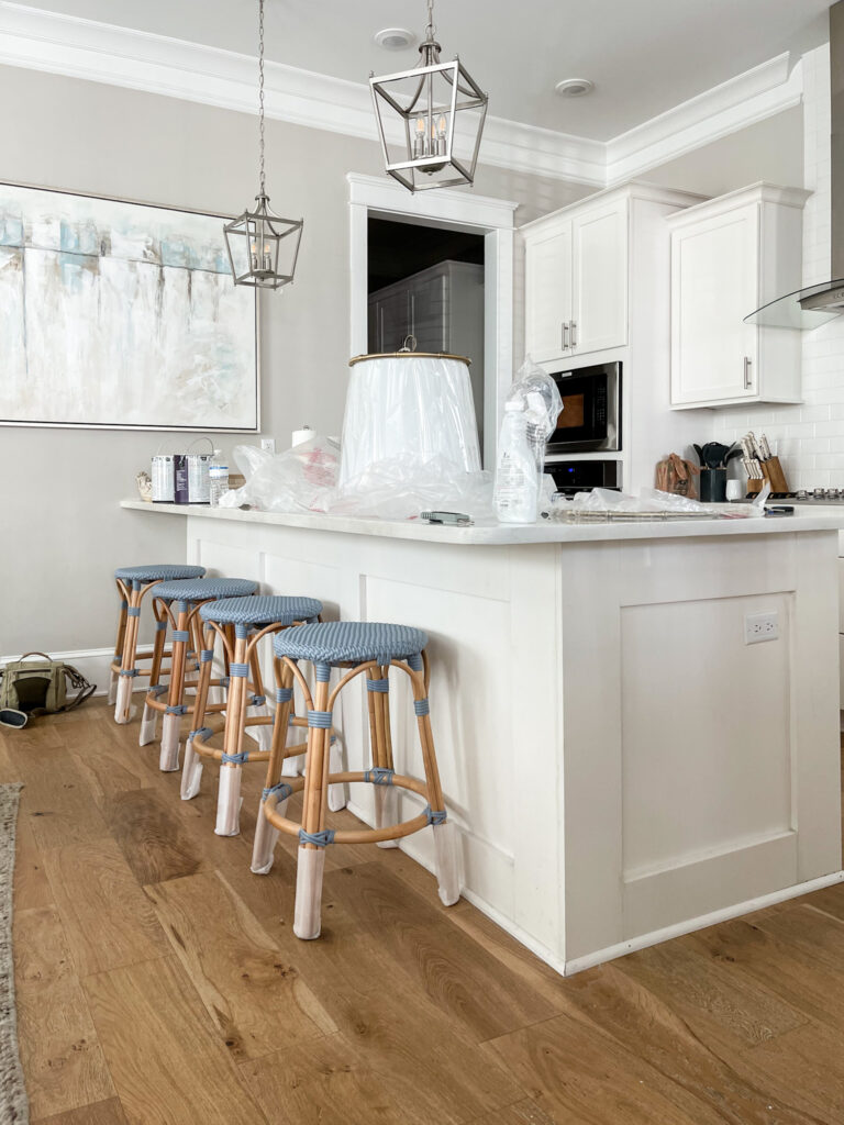Woven coastal blue backless counter stools in a white kitchen with Agreeable Gray painted walls and white oak hardwood floors.