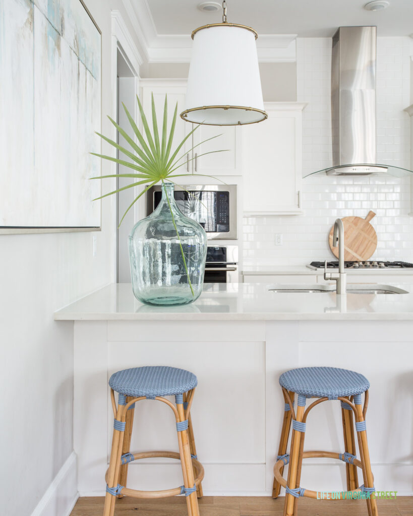 The Hola Beaches 30a kitchen updates including light blue counter stools, linen pendant lights, and a recycled glass bottle with a fan palm.